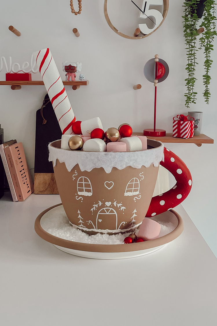 Grosse tasse marron décorée de fenêtres et cœur blanc posée sur un lit de neige artificielle