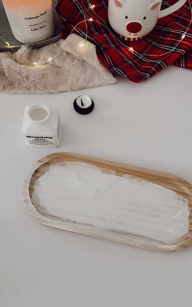 Plateau en bois recouvert d’une couche de gesso blanc, posé sur une table avec matériel autour.