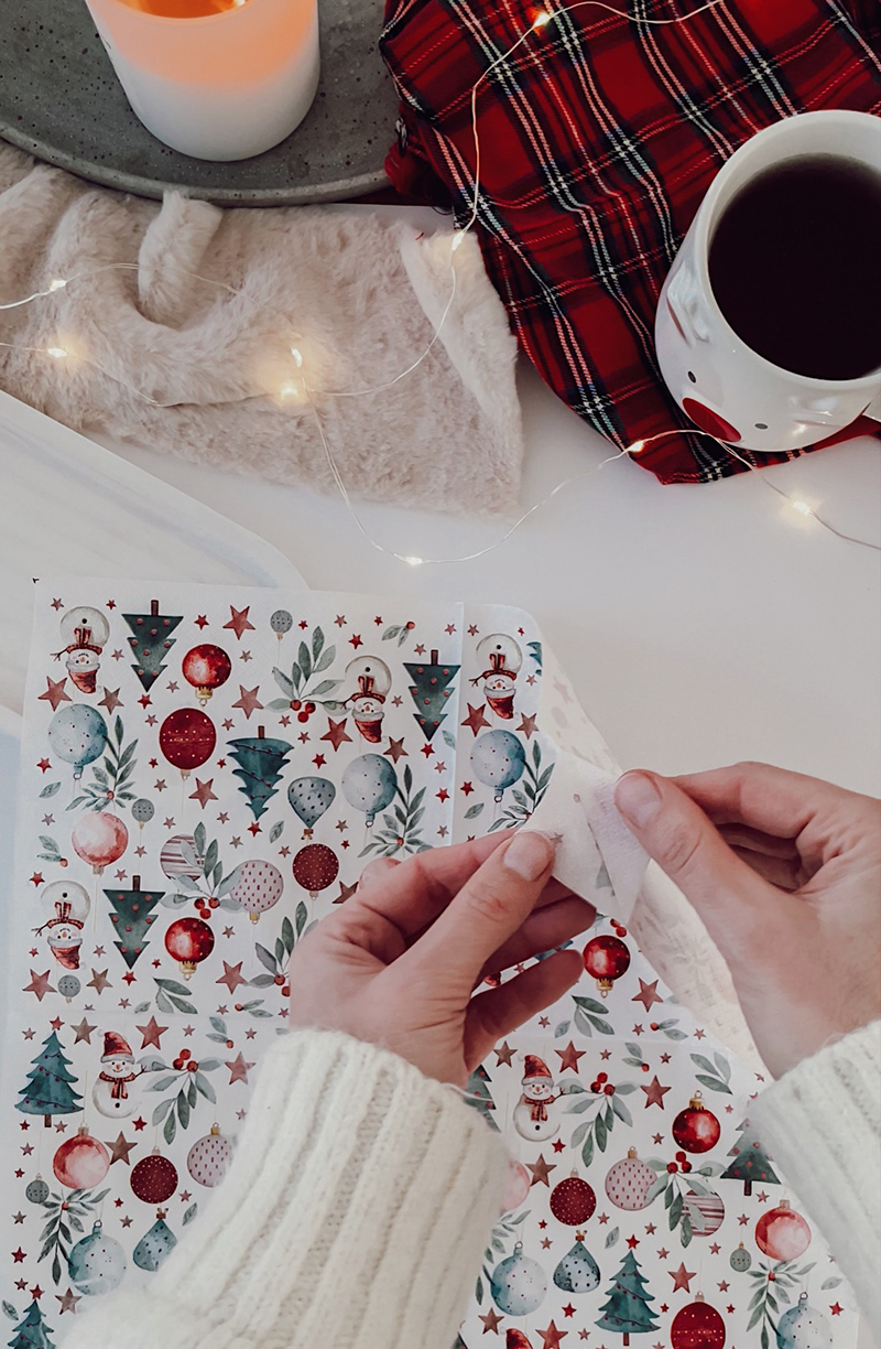 Deux mains en train de séparer les couches d’une serviette en papier décorée de motifs de Noël.