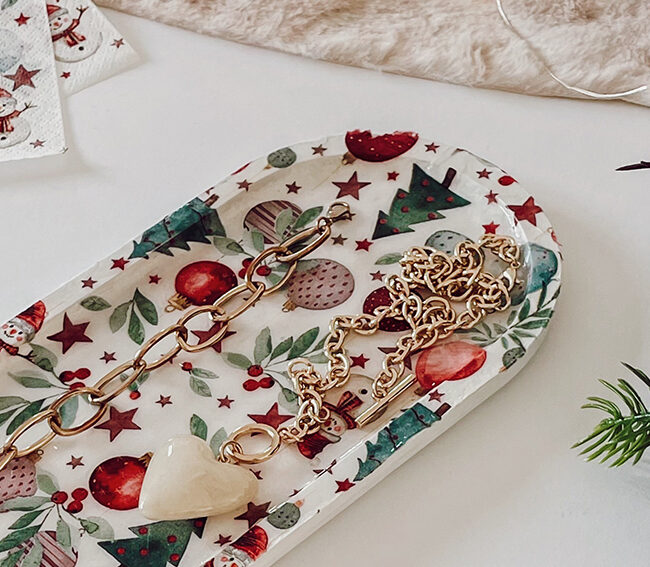 Plateau allongé décoré d’une serviette imprimée de motifs de Noël, entouré d’accessoires décoratifs.