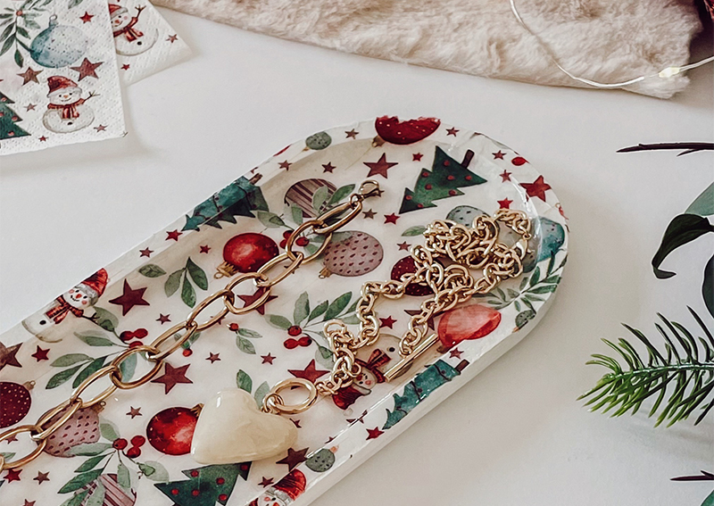 Plateau allongé décoré d’une serviette imprimée de motifs de Noël, entouré d’accessoires décoratifs.