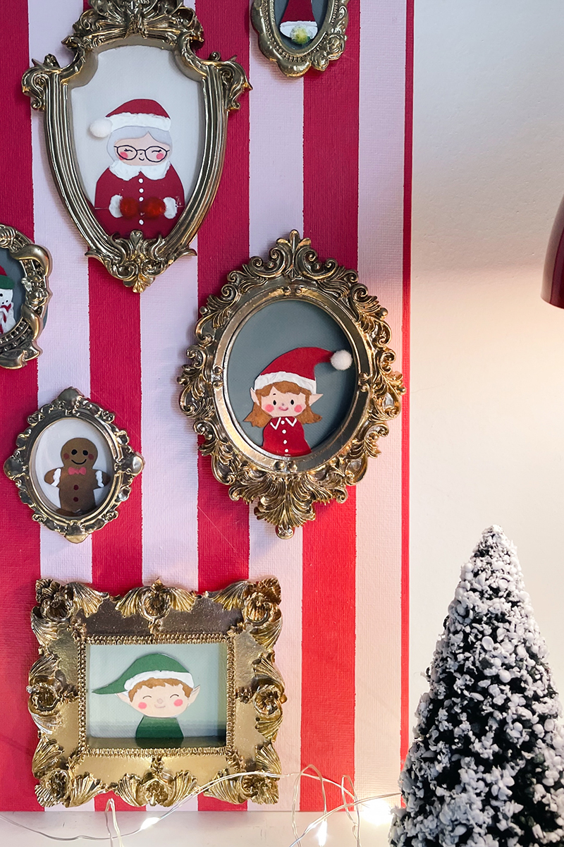 Gros plan sur plusieurs cadres dorés contenant des personnages de Noël illustrés, dont une Mère Noël, un lutin et un biscuit pain d’épice, sur fond rayé rose et rouge.