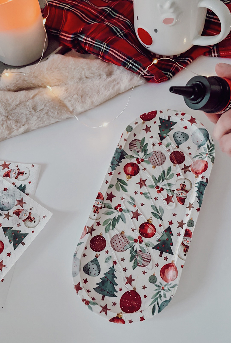 Main appliquant du gel transparent sur un plateau décoré avec une serviette de Noël.